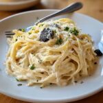 Creamy truffle pasta with parmesan and black truffle shavings on a white plate