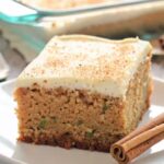 Slice of cinnamon zucchini cake with cream cheese frosting on white plate