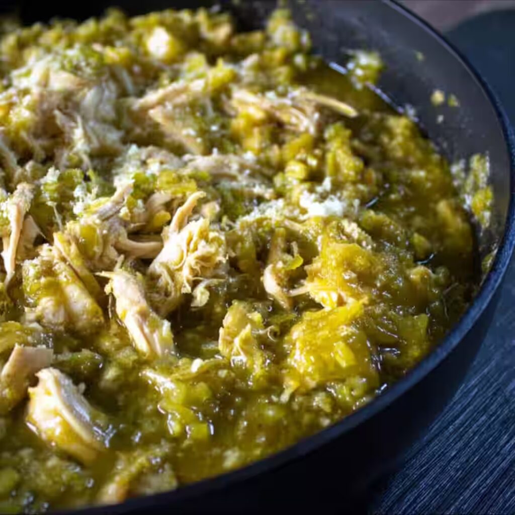 Hatch Chicken Chile Verde in a black skillet, with shredded chicken simmered in green chile sauce