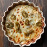 Baked Hatch Green Chile Dip in a scalloped dish with melted cheese and roasted green chiles