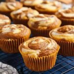 Freshly baked pumpkin cream cheese muffins with swirled cream cheese tops on cooling rack