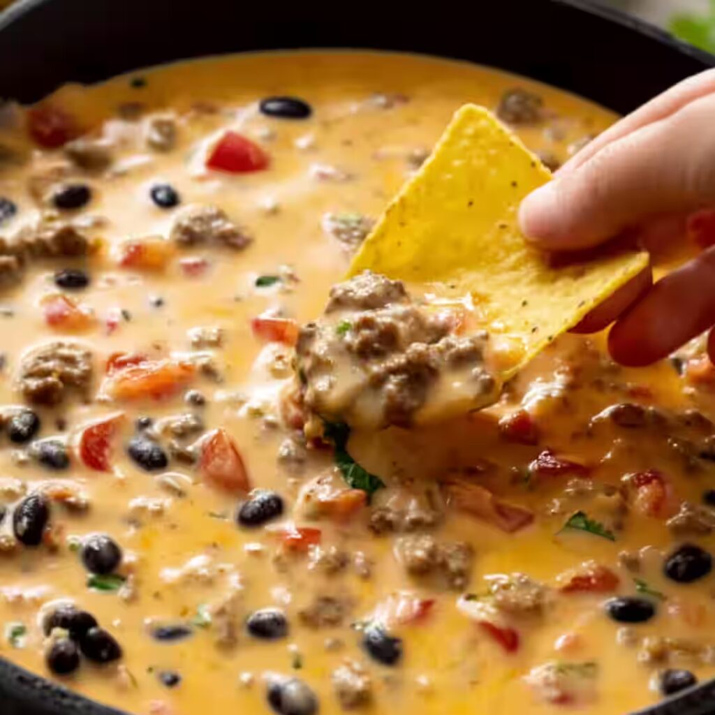 Cowboy queso in skillet with beef, beans, tomatoes, and tortilla chip