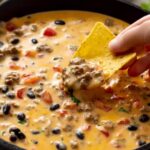 Cowboy queso in skillet with beef, beans, tomatoes, and tortilla chip