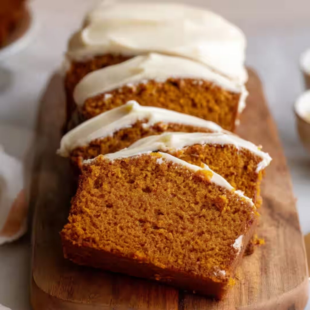 Pumpkin bread with cream cheese frosting on wooden board
