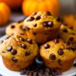 Freshly baked pumpkin chocolate chip muffins on a rustic wooden plate with fall decorations