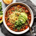 Turkey sweet potato chili topped with avocado, cheese, and cilantro in a white bowl