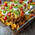 Walking Taco Casserole with beef, cheese, lettuce, tomatoes, and jalapeños in a glass baking dish