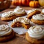 Pumpkin sugar cookies with cream cheese frosting on a rustic wooden table